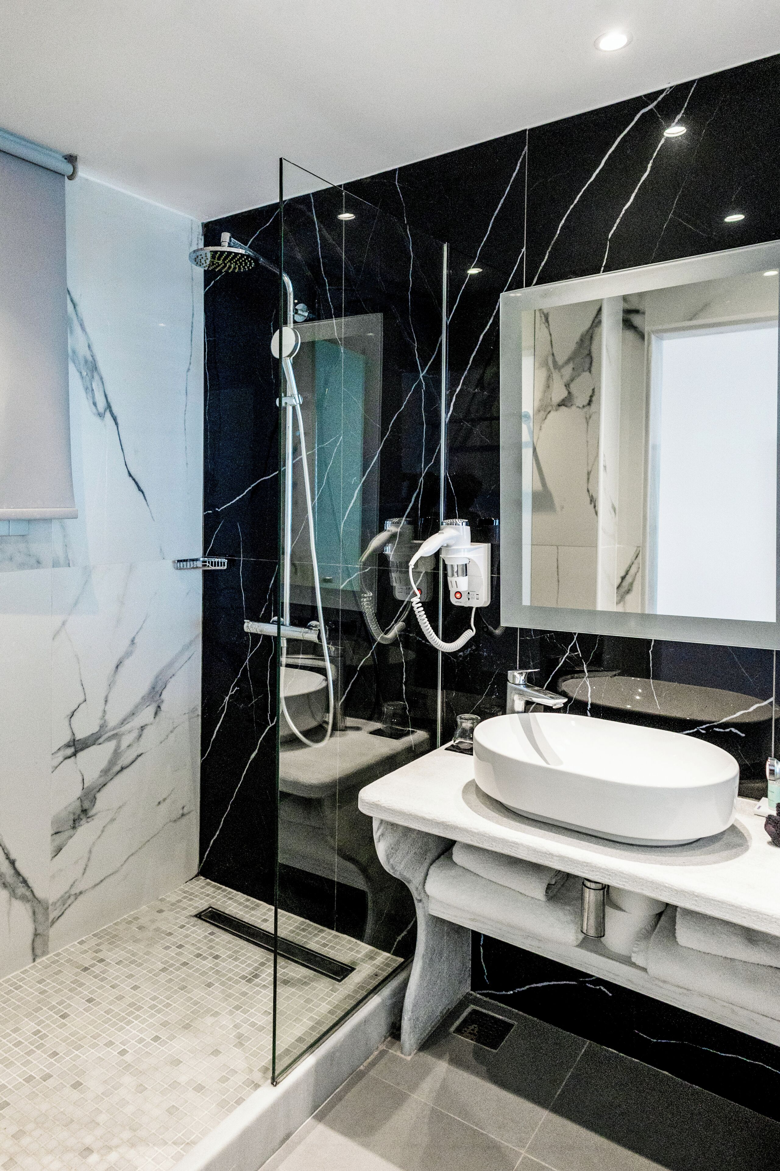 Un baño moderno con ducha envuelta en vidrio, un lavabo blanco y un espejo grande.