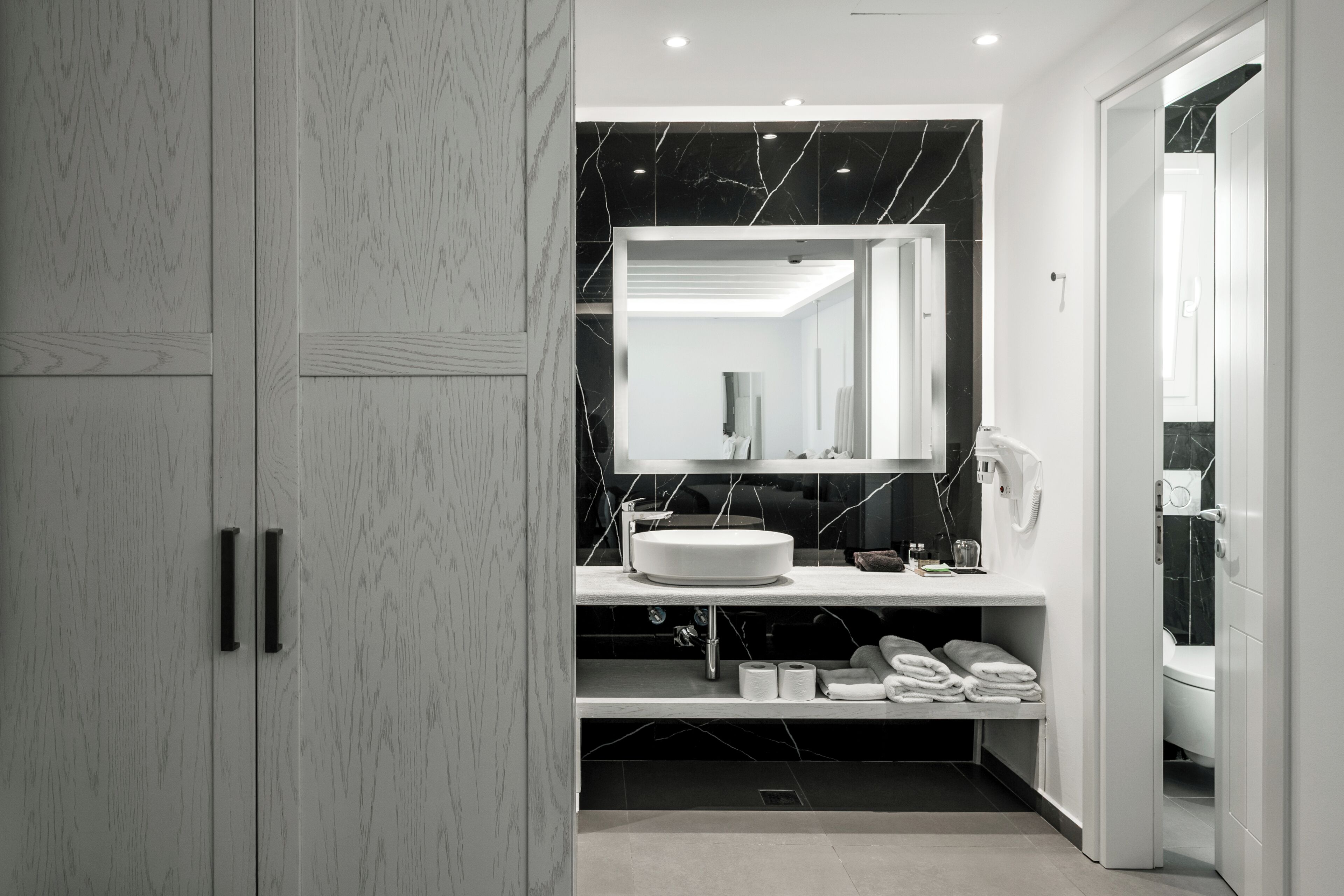 A modern bathroom with a marble vanity, a large mirror, and a toilet.