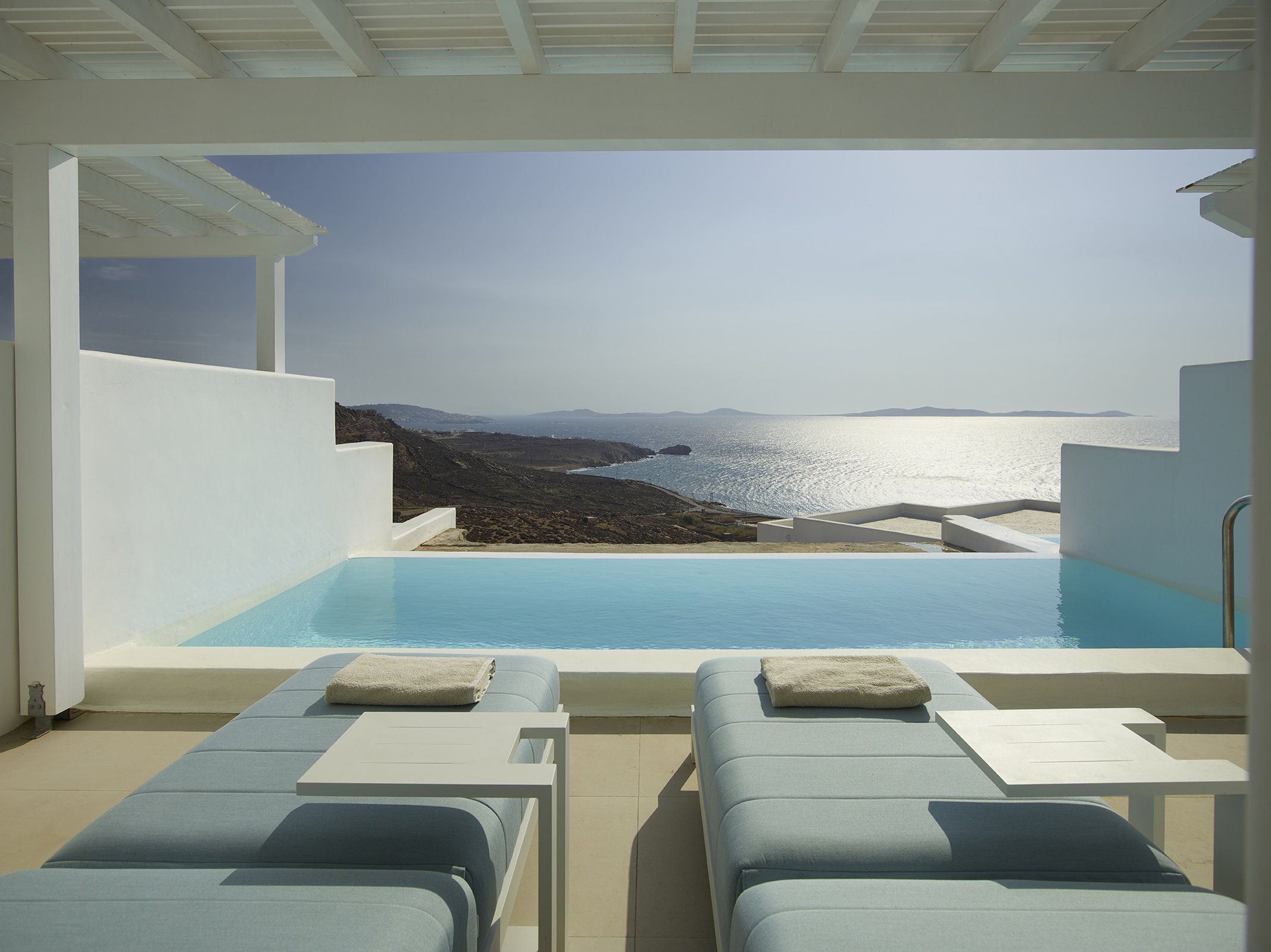 A poolside area with lounge chairs and a view of the sea and distant mountains.