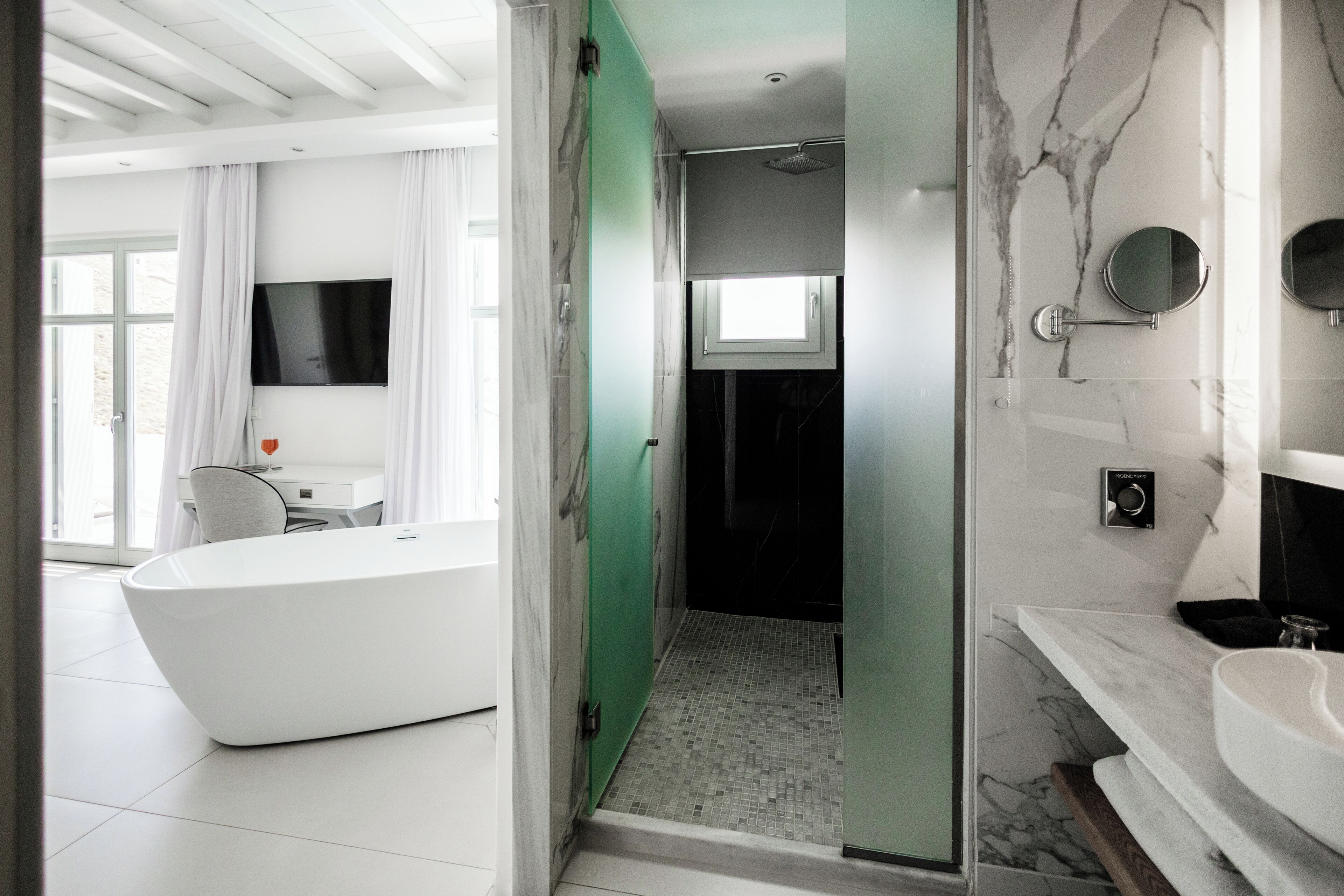 A modern bathroom with a white bathtub, a glass shower enclosure, and a marble-tiled vanity.