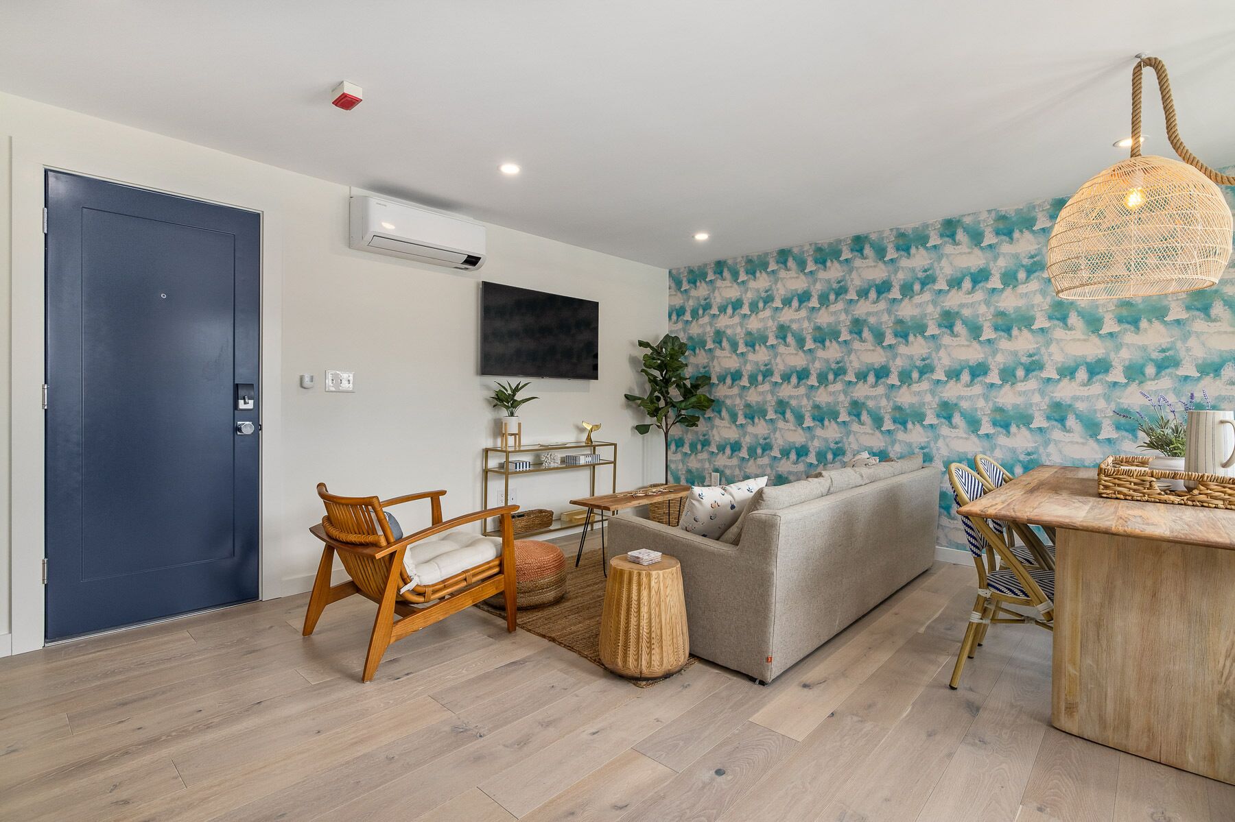 A modern living room with a grey sofa, wooden chairs, a small table, and a wall-mounted TV.
