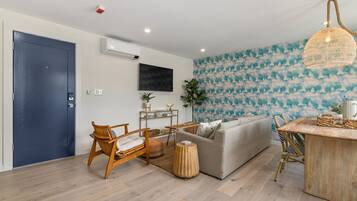 A modern living room with a grey sofa, wooden chairs, a small table, and a wall-mounted TV.