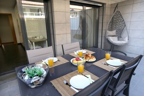 Uma mesa de jantar posta com pratos, talheres e uma tigela de frutas, com uma cadeira suspensa e um copo de suco de laranja.