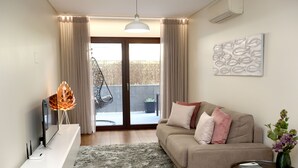 A modern living room with a sofa, a flat-screen TV, a decorative lamp, and a painting on the wall. - Like-Home - Apt 1 bedroom, with terrace - Parque das Nações (Moscavide)