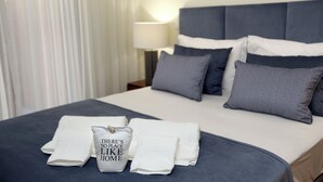 A neatly made bed with pillows and folded towels, a lamp on the nightstand, and a window with curtains. - Like-Home - Apt 1 bedroom, with terrace - Parque das Nações (Moscavide)