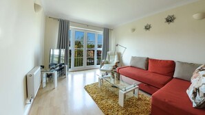 Un salon moderne avec un canapé rouge, une table basse en verre, un fauteuil blanc et une grande fenêtre avec des rideaux.