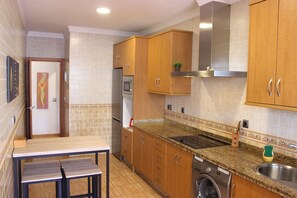 Una cocina con armarios de madera, horno empotrado, microondas, lavamanos y lavadora.