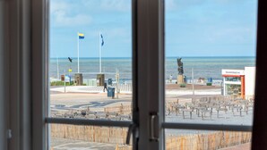 Vista desde el interior de un edificio hacia una zona de playa con una tienda de recuerdos, bancos y banderas.
