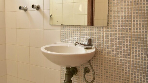 A bathroom with a white sink, a mirror, and a shower. - Triflat (Cabo Frio)