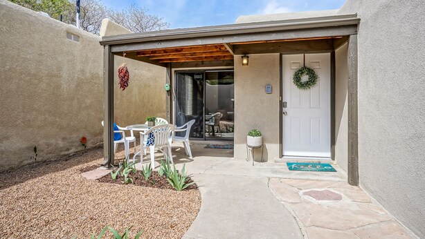 A covered patio with a table and chairs, a door with a wreath, and a small garden area. - Retro Condo in the North East Heights, 2bd/1ba, garage, Pet friendly (Albuquerque)