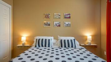 Une chambre d’hôtel avec un lit recouvert d’une courtepointe à pois, deux lampes de chevet et six tableaux encadrés accrochés au mur.