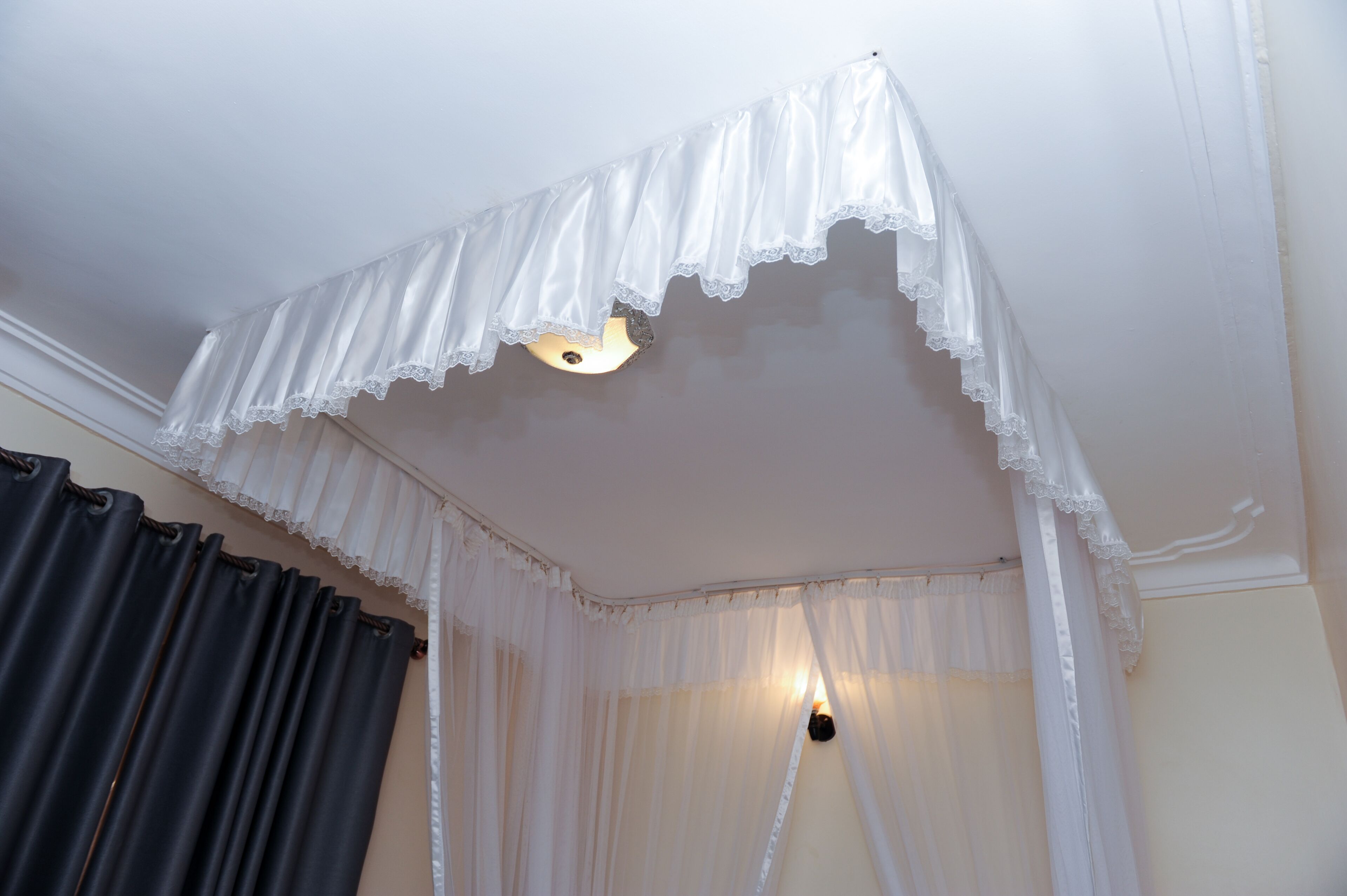 A room with a white canopy bed, a light fixture, and a window with curtains.