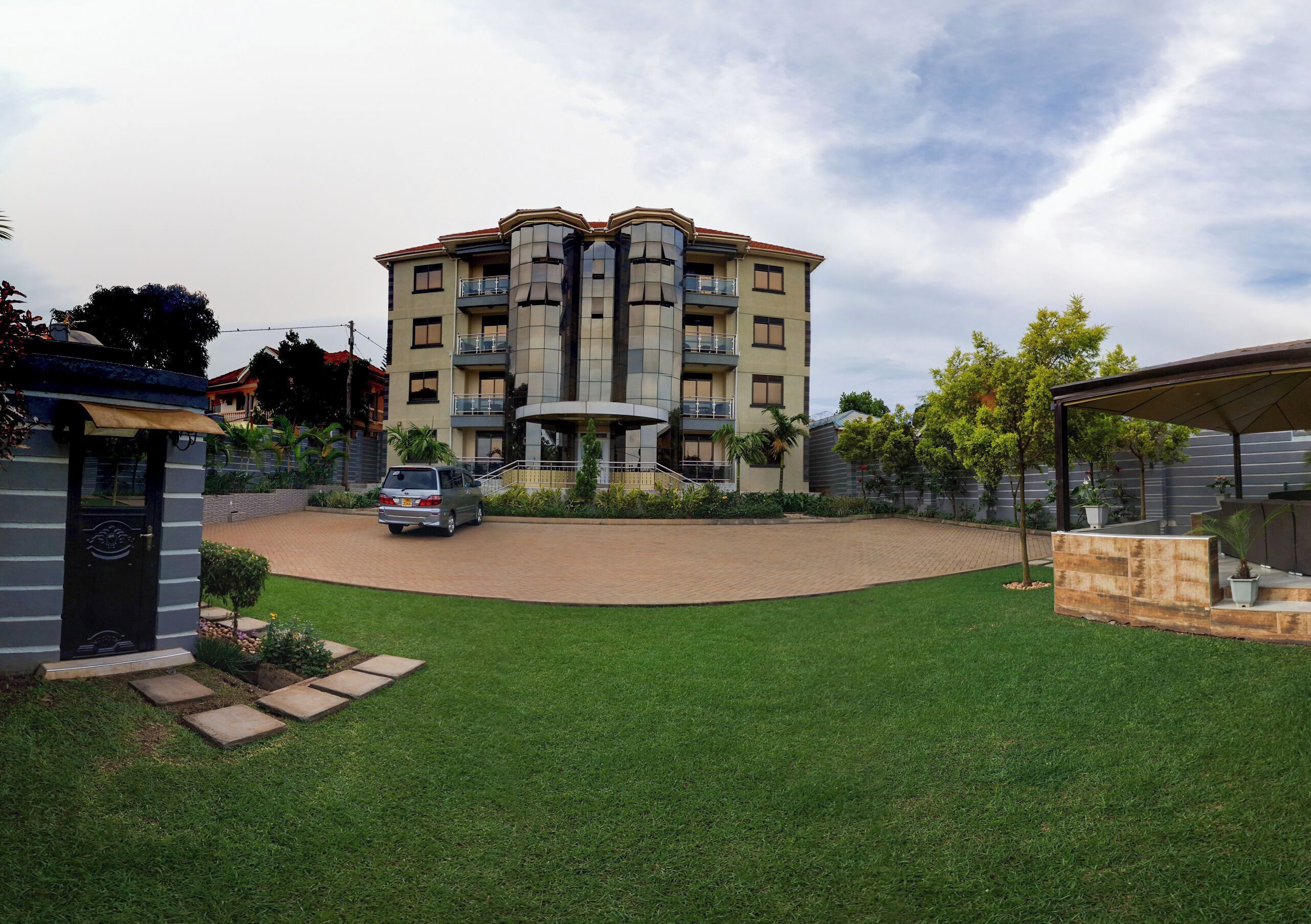 Un edificio residencial de varios pisos con un patio central, un automóvil estacionado en la entrada y un césped cuidado.