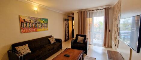 Una sala de estar con un sofá, sillones, una mesa de centro, un cuadro y un televisor.