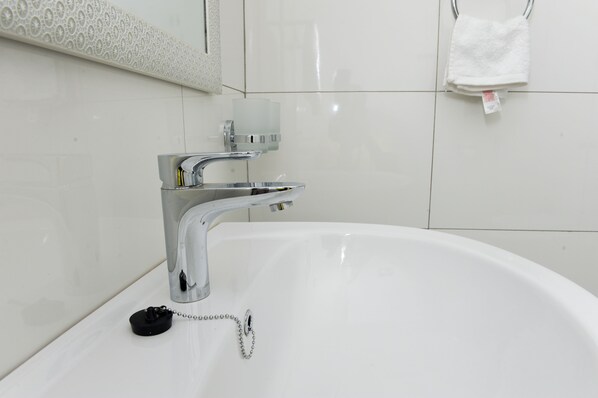 A white bathtub with a chrome faucet and a black stopper. - Eric Wilkins Apartments (Kampala)