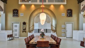 A spacious dining area with a long wooden table and leather chairs, a chandelier, and a staircase with a white railing. - Church conversion for a unique stay and experience: 5 bedrooms and 5 bathrooms (Rinsumageest)