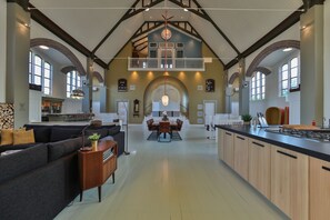Una cocina amplia con una isla central, un comedor con techo alto y vigas a la vista, y una zona de estar acogedora con un sofá y una mesita auxiliar.
