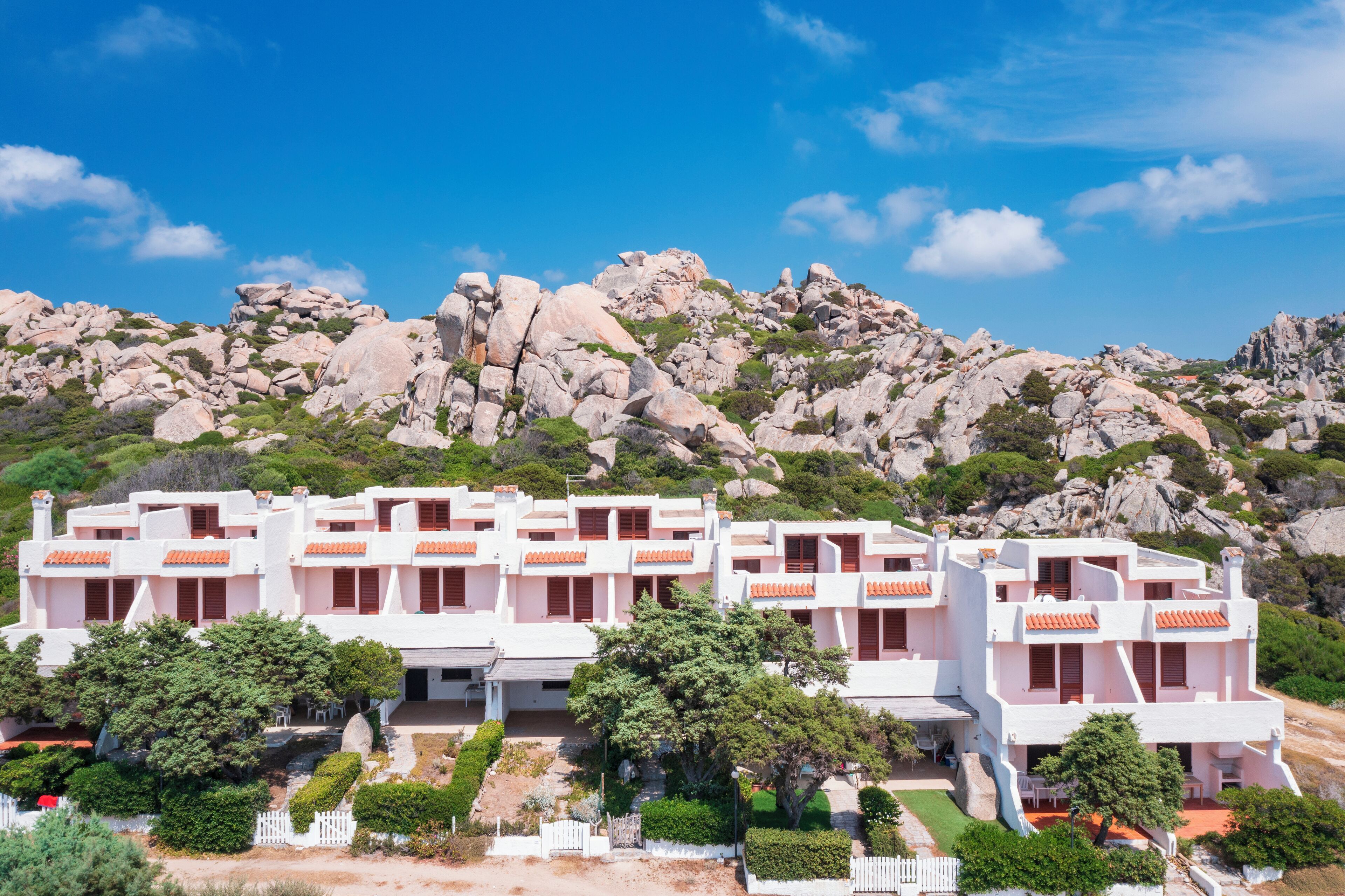 A white building with red accents, surrounded by greenery and rocky terrain.