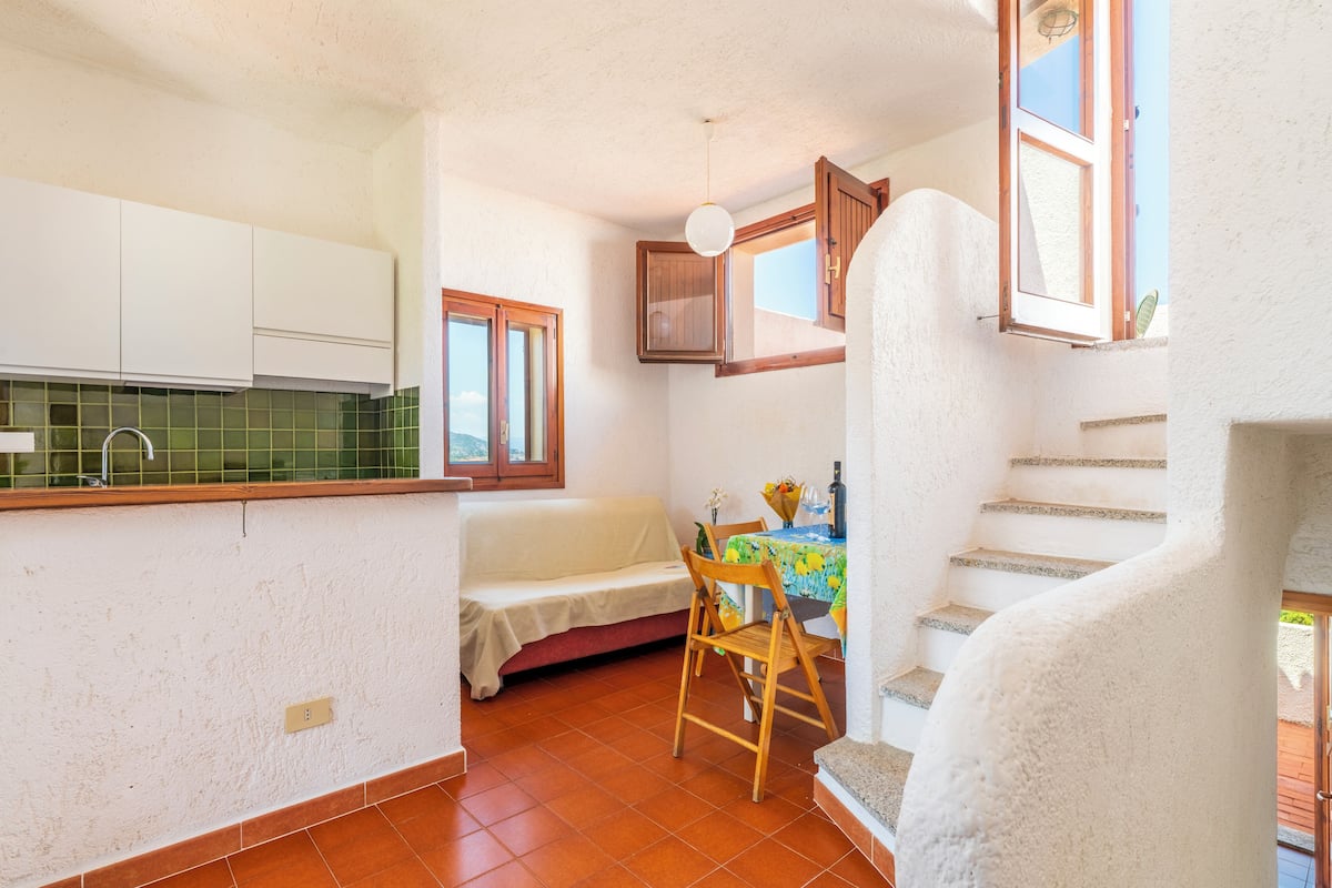 Una cocina compacta con armarios blancos, una mesa de comedor con mantel colorido y un pequeño sofá.