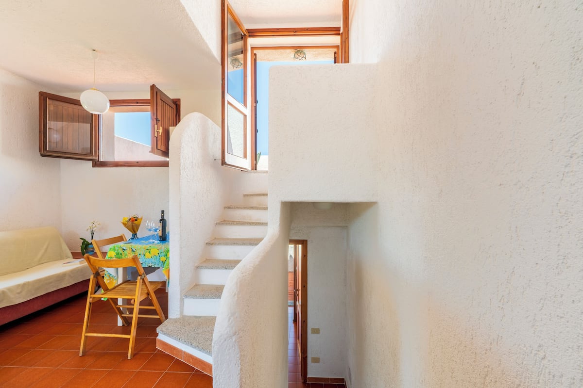 Un espacio habitable compacto con una escalera, un comedor con mesa y sillas, y un sofá.