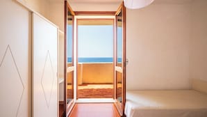 A room with a bed, a view of the sea, and a door leading to a balcony.