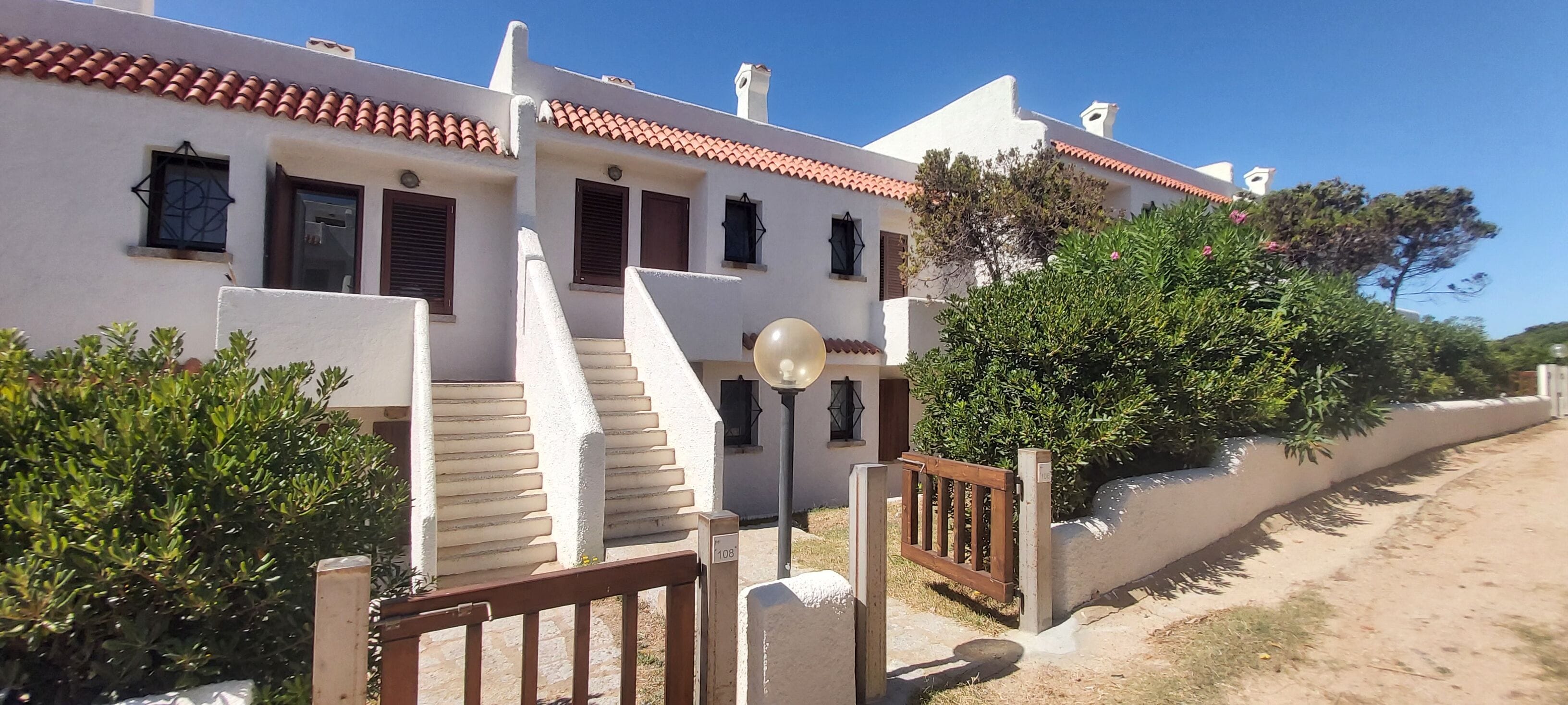 A two-story building with a white facade, red-tiled roof, and a staircase leading to the entrance.
