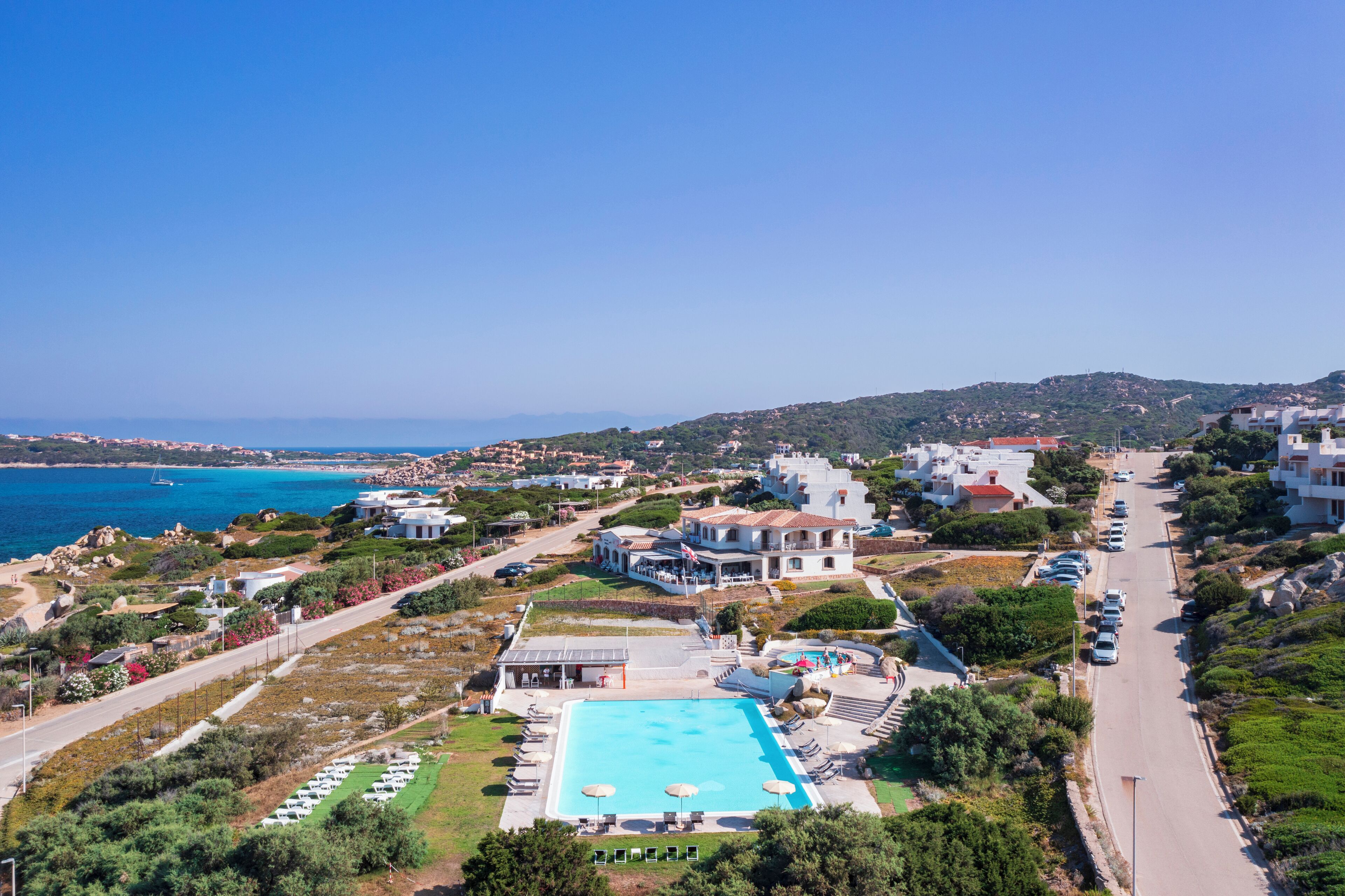 A coastal property with a swimming pool, multiple villas, and a road leading to the sea.