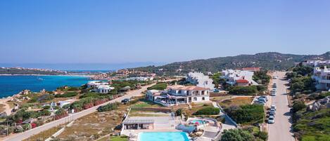 A coastal property with a swimming pool, multiple villas, and a road leading to the sea.