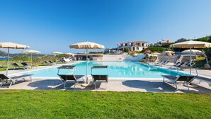 A swimming pool with lounge chairs and umbrellas, surrounded by greenery and buildings.