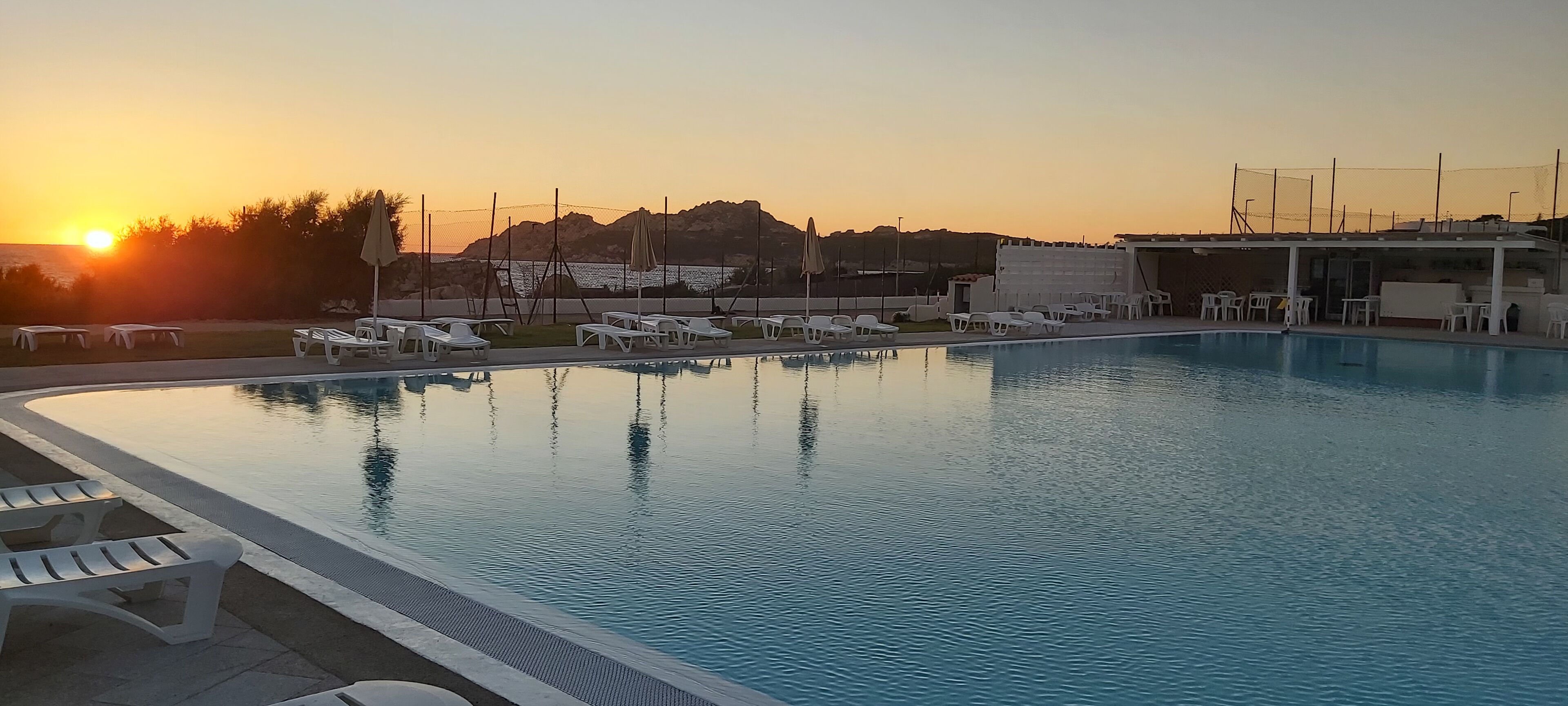 Una piscina con sillones de descanso y vistas al atardecer.