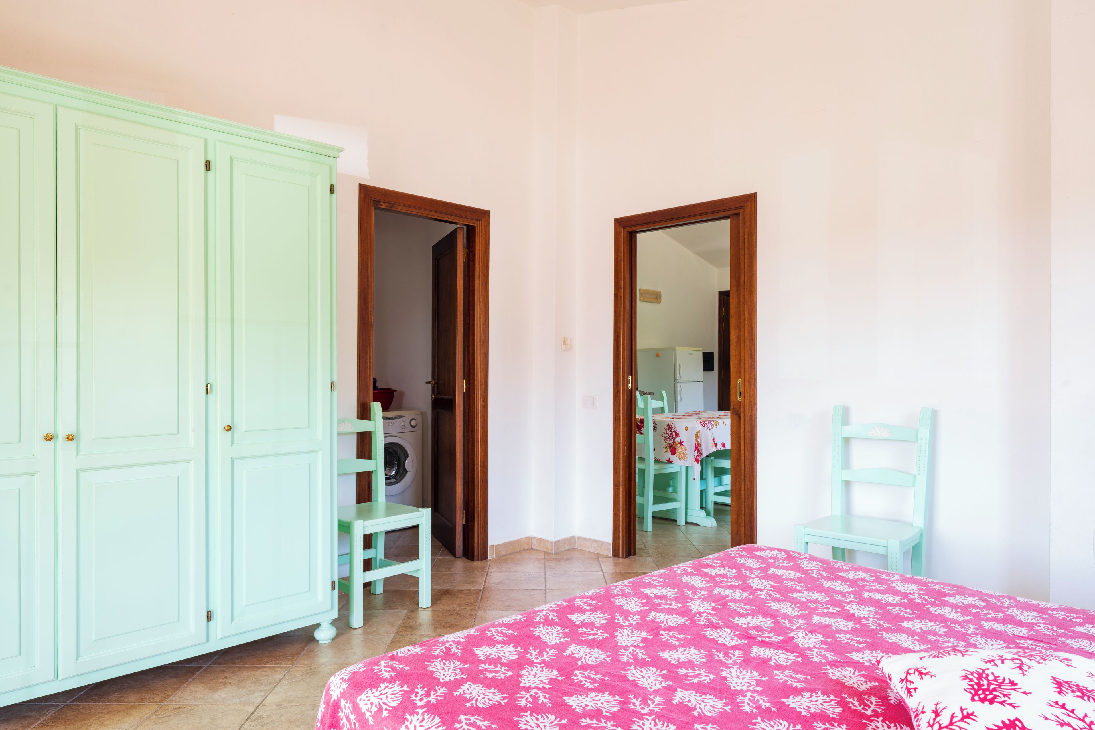 Ein Schlafzimmer mit einem Bett, einer Waschmaschine und einem Essbereich, der durch eine offene Tür sichtbar ist.