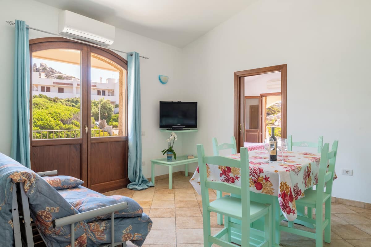 Una habitación con sofá, mesa de comedor con sillas, televisión y vistas a zonas verdes.