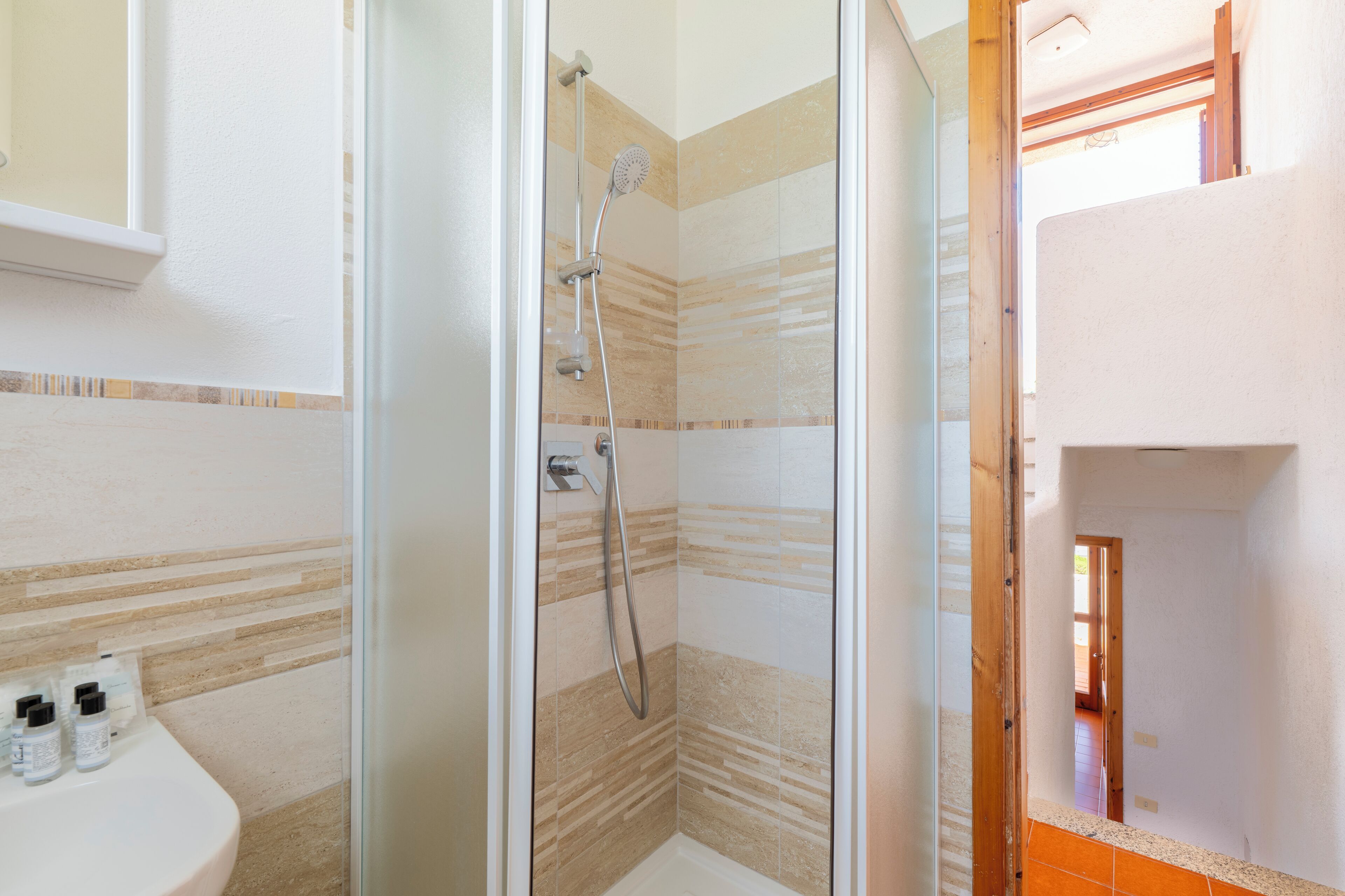 A glass-enclosed shower with a handheld showerhead, a wall-mounted faucet, and a tiled floor.