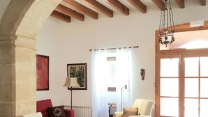 A living room with a red sofa, a white armchair, a beige armchair, and a wicker chair. There is a painting on the wall, a floor lamp, and a window with curtains. - CASA DE L'ARTISTA - CAN ROCA (Alcúdia)