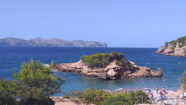 A coastal scene with rocky outcrops, clear blue sea, and distant mountains. - CASA DE L'ARTISTA - CAN ROCA (Alcúdia)