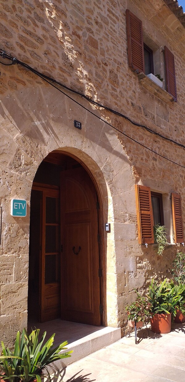 Un edificio de piedra con puerta de madera y ventanas con contraventanas, un letrero con el número 13 y un cartel que indica servicio ETV.
