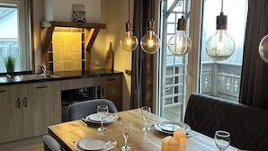 A modern kitchen with wooden cabinets, a dining table set for four, and pendant lights.