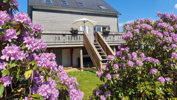 A two-story house with a grey roof, a wooden deck, and a staircase leading to the upper floor.