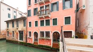 Un edificio junto a un canal con fachada rosa, varias ventanas y un balcón con plantas.