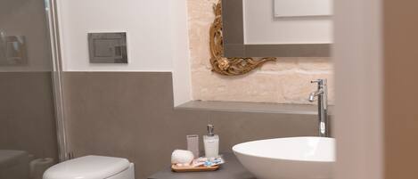 Un baño moderno con inodoro blanco, un lavamanos grande y blanco, y un espejo sobre el lavamanos.