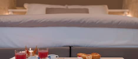 A neatly arranged breakfast tray with pastries, a glass of red juice, and small bowls of cream on a table in front of a bed.