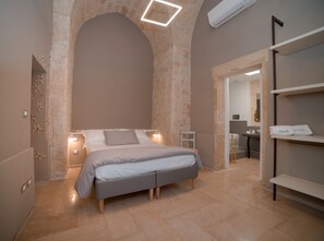 A modern bedroom with a large bed, stone walls, and a built-in bench. - Litium 3 (Lecce)