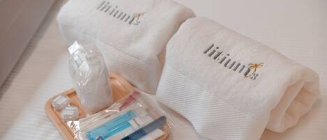 A neatly folded white towel with the word "liminus" embroidered on it, placed on a bed.