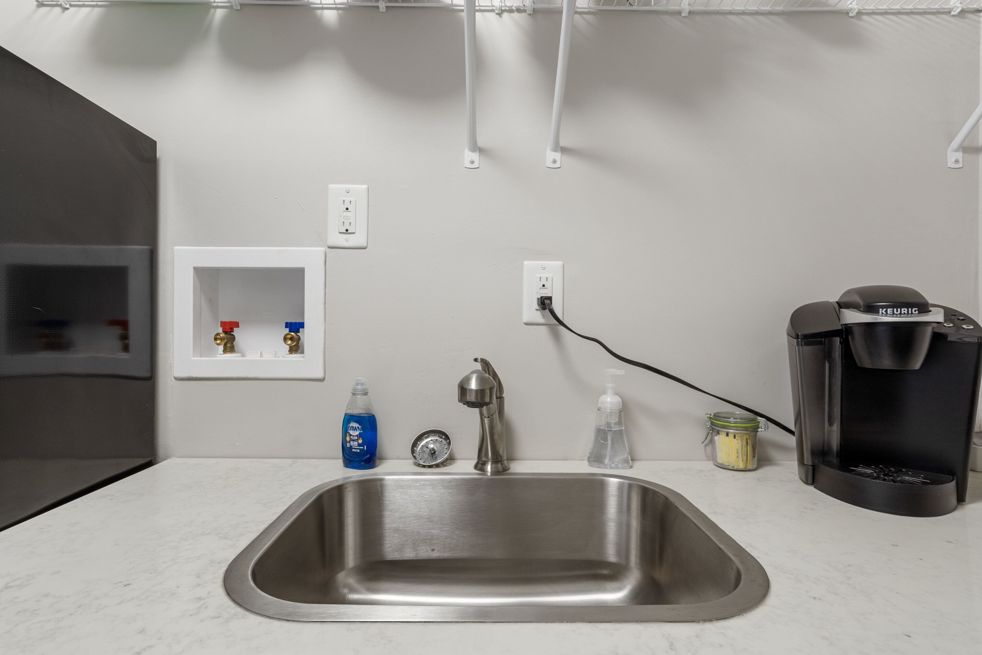 A kitchen with a stainless steel sink, a coffee maker, and a bottle of dish soap.