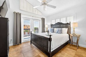 Ein Schlafzimmer mit Bett, Deckenventilator, Fenster mit Jalousien, Lampe und Blick ins Freie.