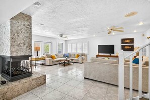 A spacious living room with a stone fireplace, a flat-screen TV, and a staircase.