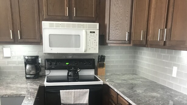 A compact kitchen with wooden cabinets, a white microwave, a stove, and a coffee maker. - Shuttle Bus. Picturesque. King Bed. Updated. Parking (Keystone)