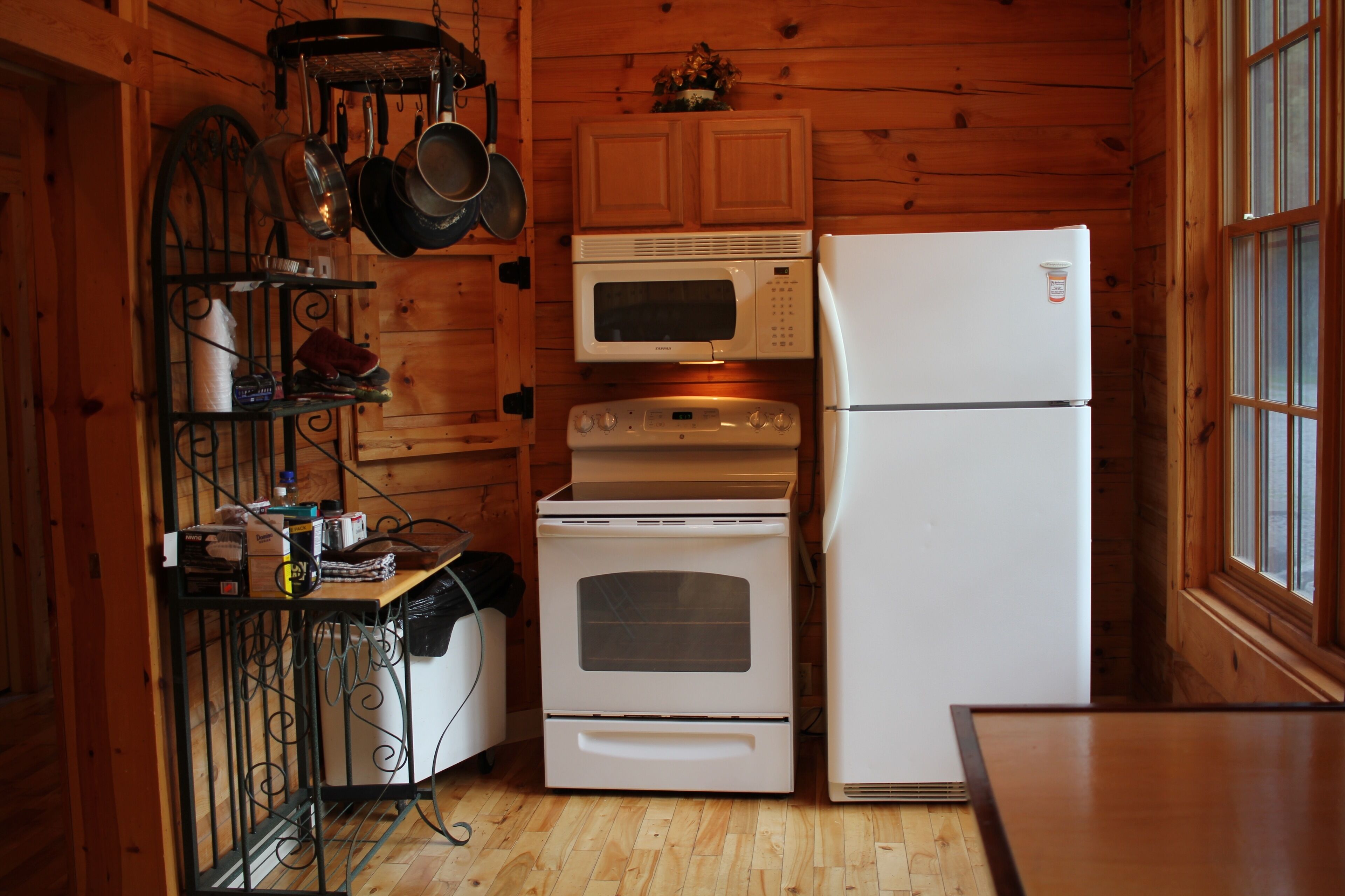 A compact kitchen with wooden walls, a microwave, oven, and refrigerator.