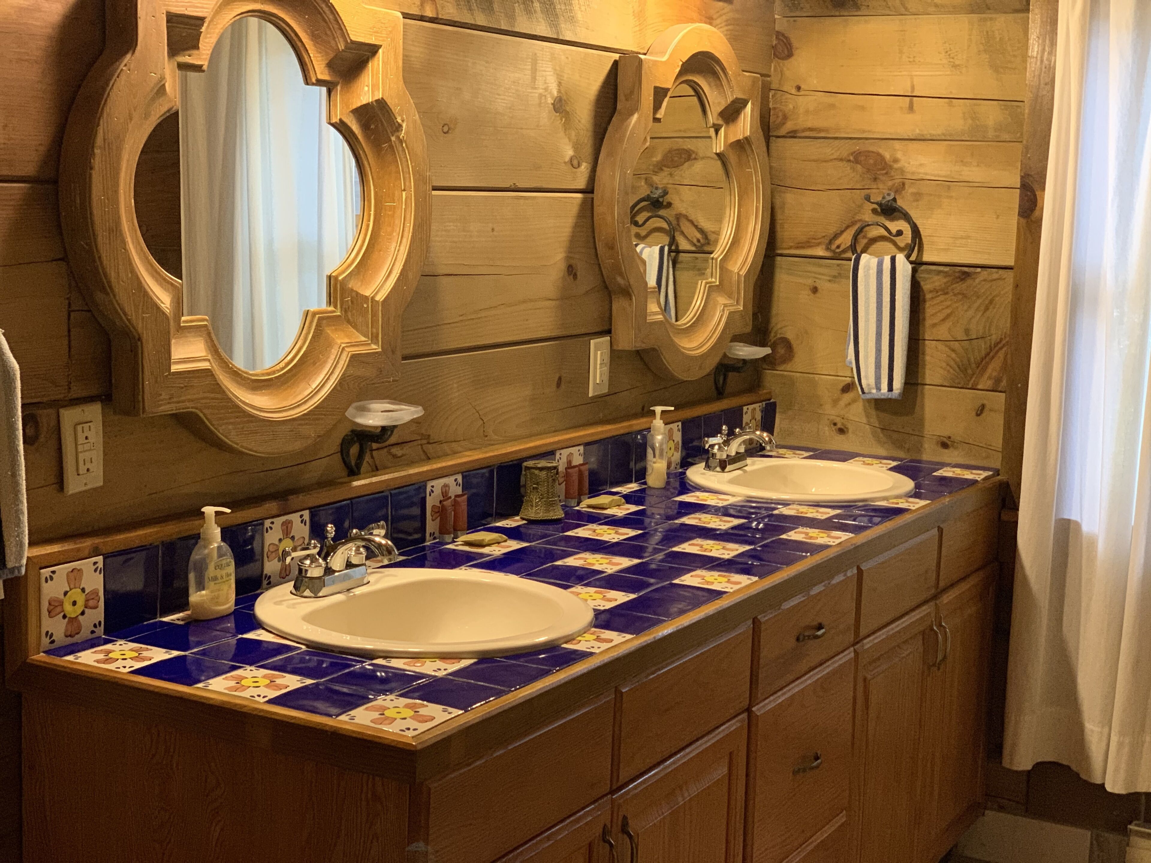 Un baño con paredes de madera, dos lavamanos y espejos decorativos.