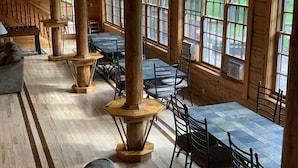 A wooden cabin interior with multiple dining tables and chairs, large windows, and a staircase. - Elk Springs Resort (Monterville)